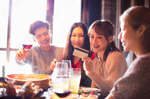 happy young group showing credit card and chatting in restaurant
