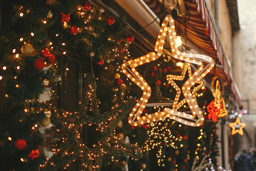 Christmas street decor. Stylish christmas golden star illumination and fir branches with red and gold baubles, golden lights bokeh on front of building at holiday market in city street
