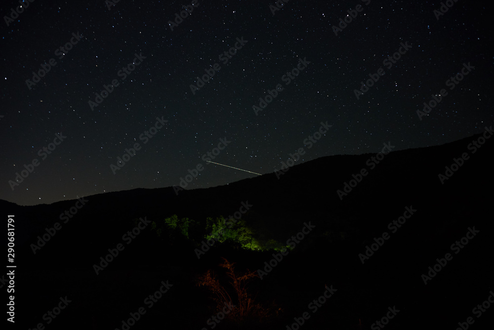 A meteor flies in the starry night sky among the mountains.