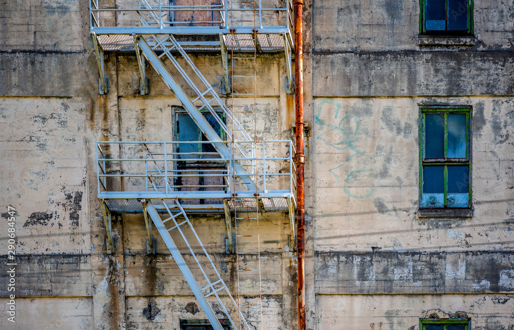 Wall of an old abandoned industrial building with windows and a fire staircase