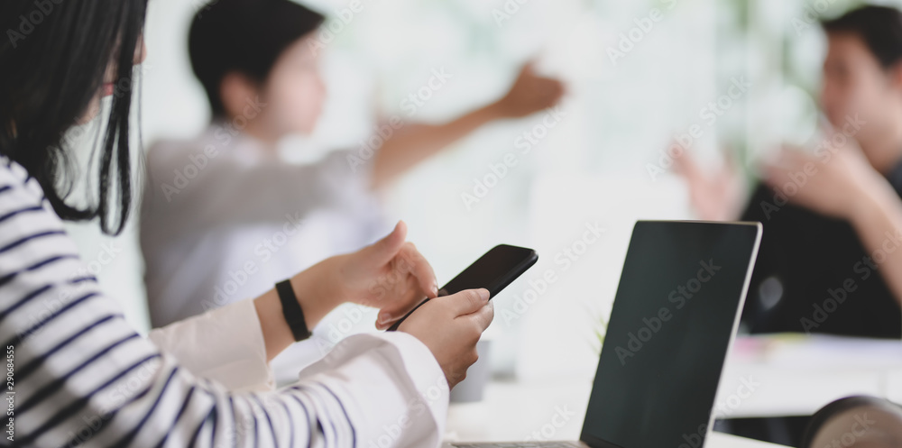 Young female freelancer working on blank screen smartphone with her team members