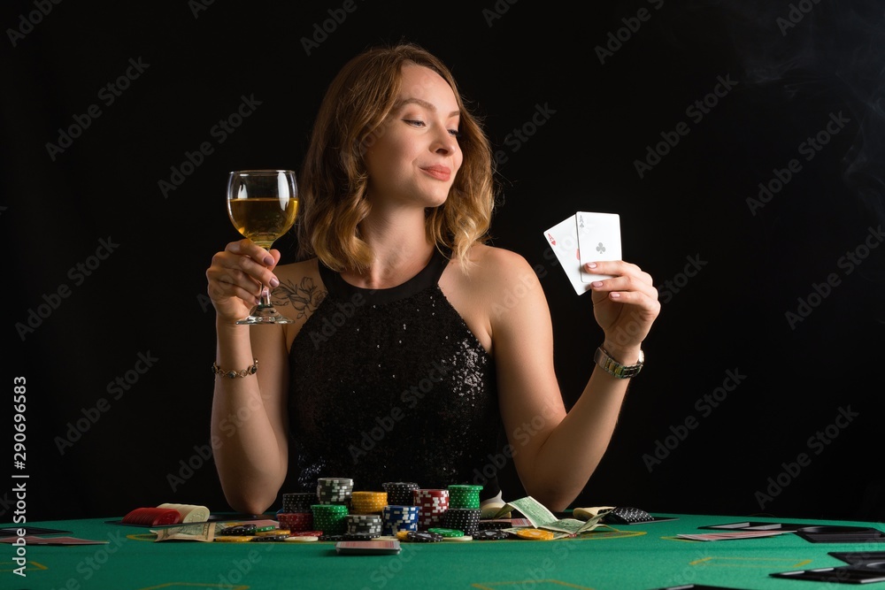 A young girl in a black evening dress plays poker in a casino. Game business and success on a black background with smoke, horizontal photo A young girl in a black evening dress plays poker in a casino. Game business and success on a black background with smoke, horizontal photo