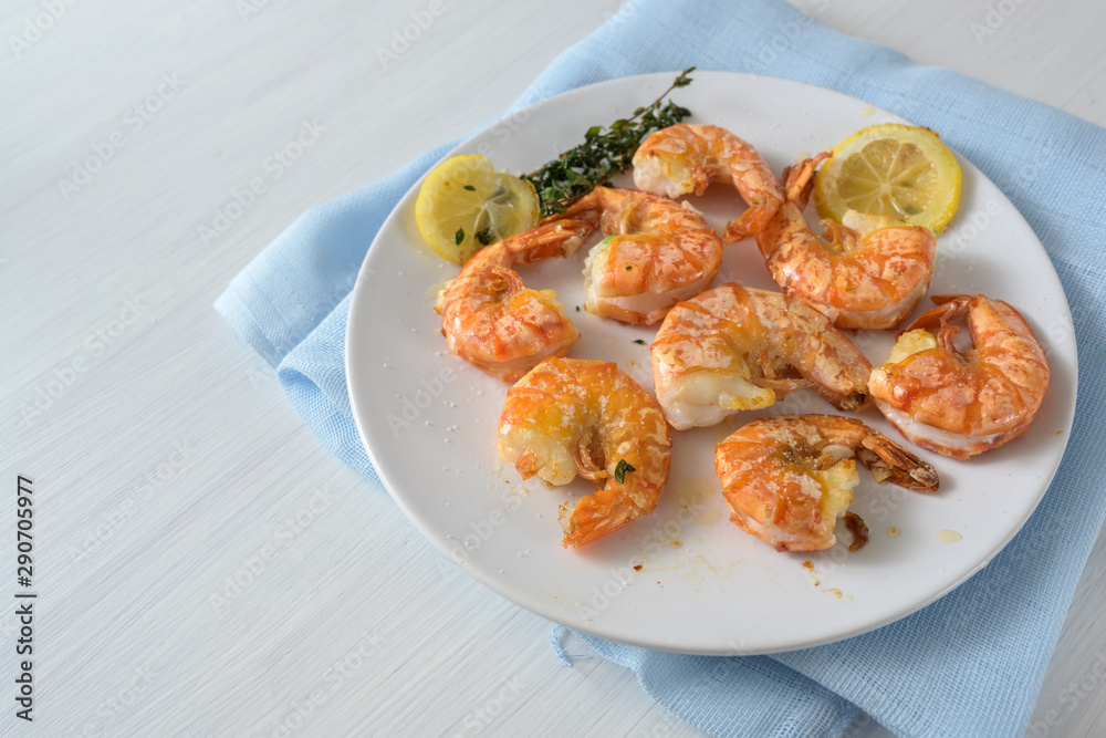 Roasted tiger prawn shrimps with garlic, lemon and herbs on a white plate, copy space