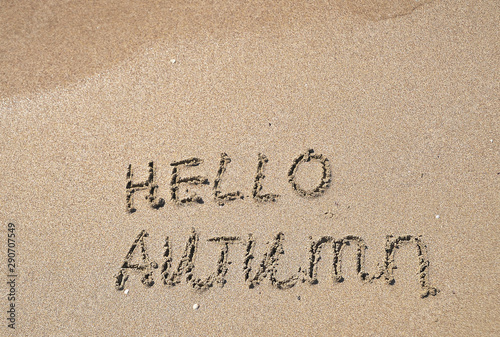 The words Hello autumn written on sand.