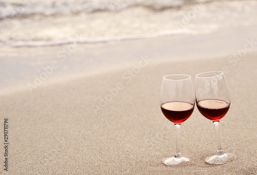 Glasses with red wine on the beach at sunset. Romantic concept.