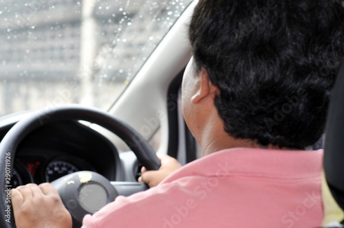 A man wearing a pink shirt was driving on a rainy day.