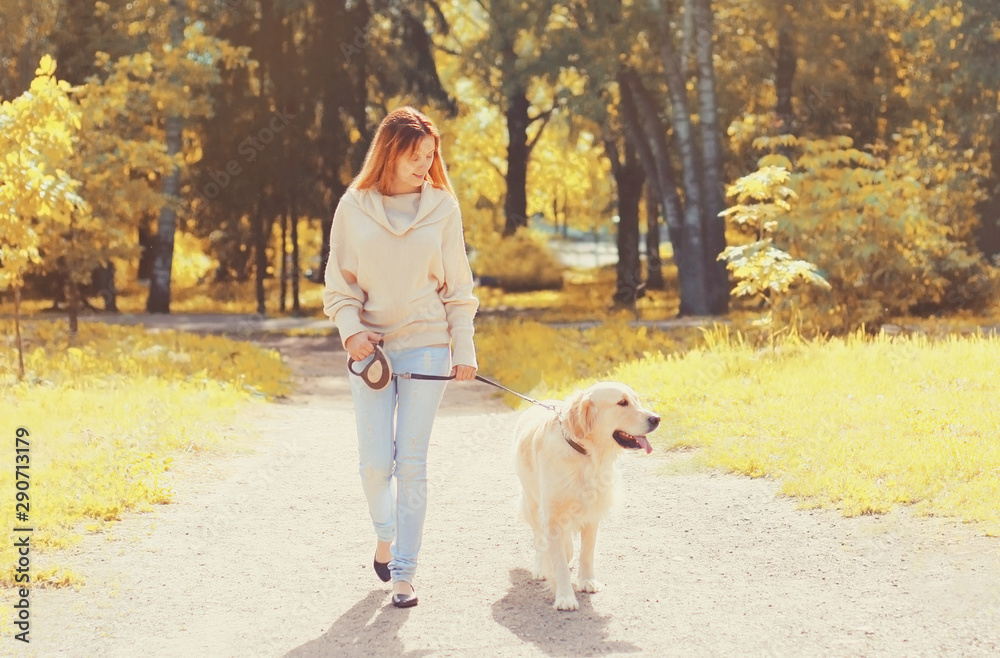 Young woman walking with her Golden Retriever dog on leash in sunny autumn day