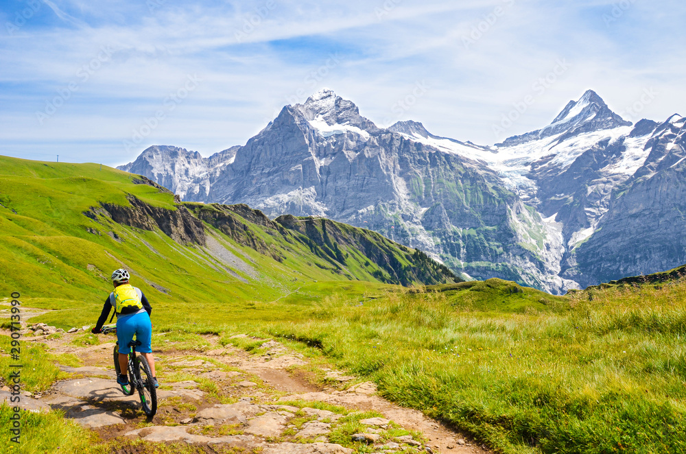 Mountain biker riding downhill in the Swiss Alps. Famous mountains Jungfrau, Eiger and Monch in the background. Mountain biking, cycling in the Alps. Cyclist with a helmet. Active, outdoor sports