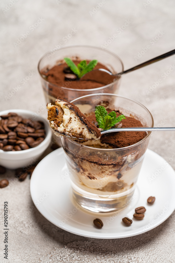 Portion of Classic tiramisu dessert in a glass cup on concrete background Portion of Classic tiramisu dessert in a glass cup on concrete background