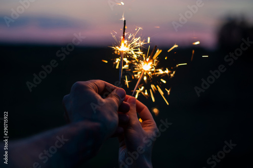 Hands holding sparkling fireworks to the sky at twilight