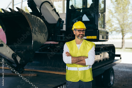 worker standing arms crossed in front of excavator machine