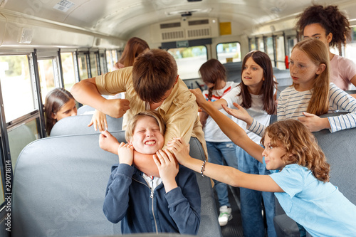 Classmates going to school by bus boy strangling kid angry while others trying to stop him photo