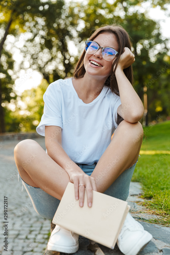 Smiling young girl holding a book while sitting in the park Smiling young girl holding a book while sitting in the park