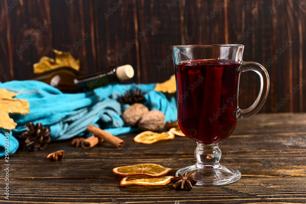 Cup of mulled wine with spices, bottle, scarf, dry leaves and oranges on a wooden table. Autumn mood, method to keep warm in the cold, copy space.