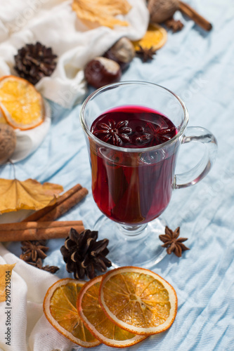 A cup of mulled wine with spices, dry leaves and oranges on the table. Autumn mood, a method to keep warm in the cold, copy space, morning light.