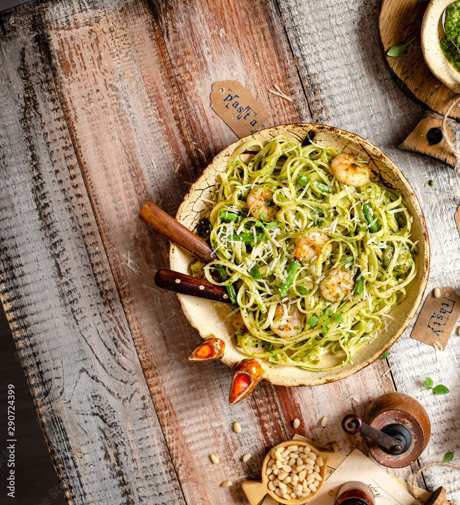 overhead shot of tasty homemade italian pasta with grilled shrimps, pesto sauce, parmesan cheese, fresh basil in ceramic bowl on wooden rustic table overhead shot of tasty homemade italian pasta with grilled shrimps, pesto sauce, parmesan cheese, fresh basil in ceramic bowl on wooden rustic table