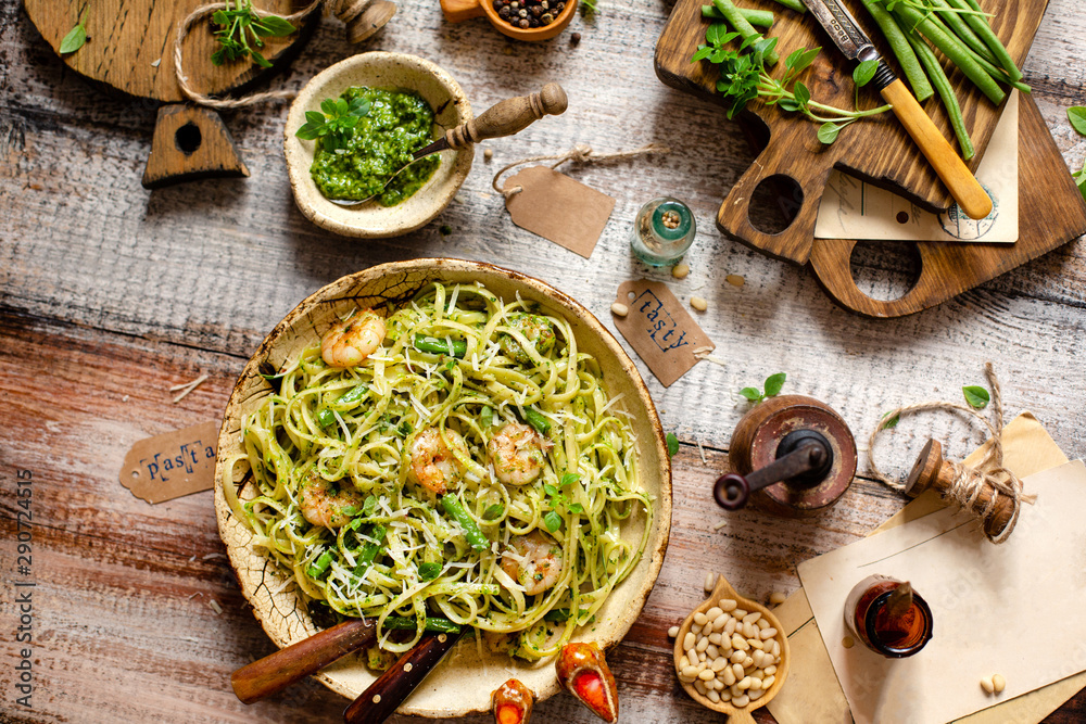 overhead shot of tasty homemade italian pasta with grilled shrimps, pesto sauce, parmesan cheese, fresh basil in ceramic bowl on wooden rustic table