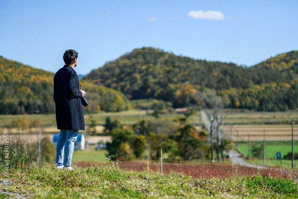 A man stading on the hill  with camera looking at the landscape of countryside.