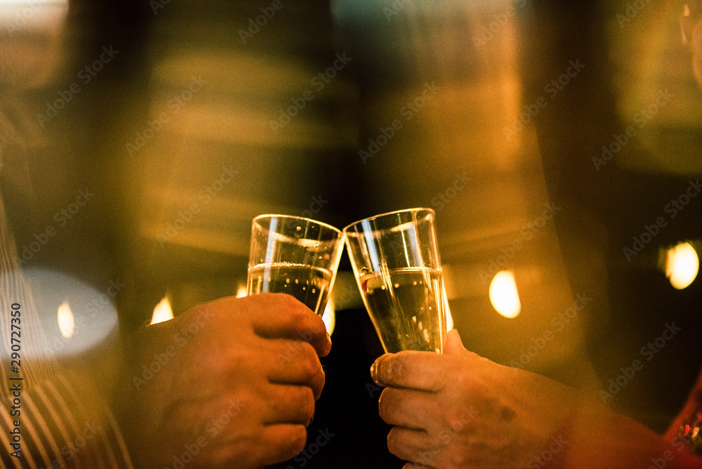 close up of two hands with glass with champagne clinking together to celebrate the new year or something party alones
