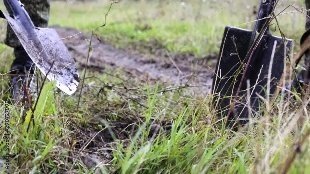 Three military soldiers bury a mine with earth with a shovel in a Chernobyl field Three military soldiers bury a mine with earth with a shovel in a Chernobyl field