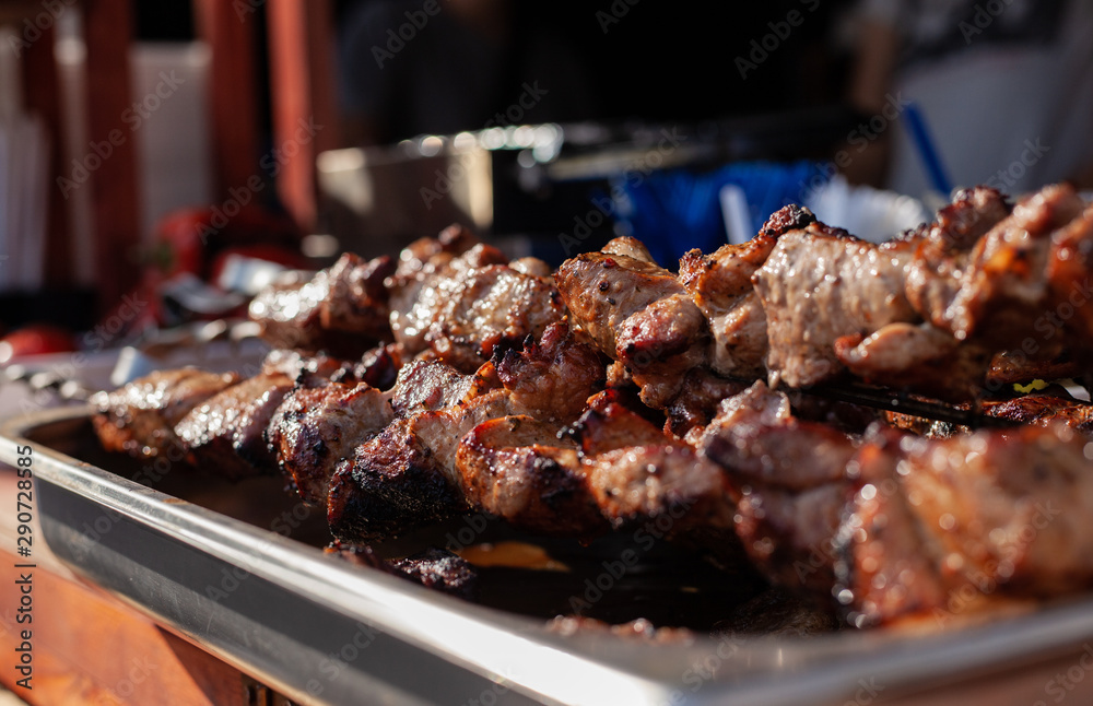 Roasted meat on a skew is on the table next to fried potatoes and vegetables in the open air