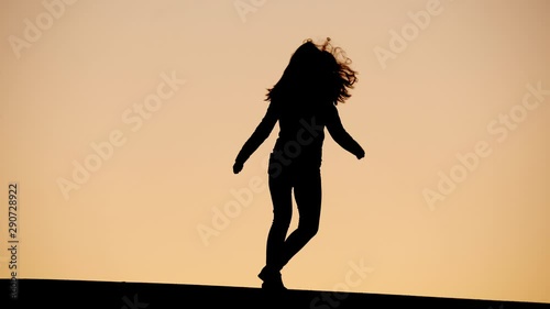 Excited young woman come jumping, hop up and turn around on place. Black silhouette against sunset sky, quick shot of happy person, dancing in high spirits photo