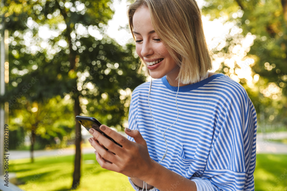 Image of blonde cheerful woman using cellphone and earphones Image of blonde cheerful woman using cellphone and earphones