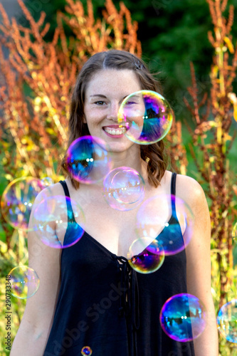 young brunette woman standing outdoors with soap bubbles