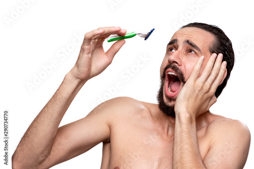 Frightened bearded man with mustache looks at the old shaving stick standning bare isolated over white background. Concept of morning treatment and shaving. Time to trim your beard. Morning routine.