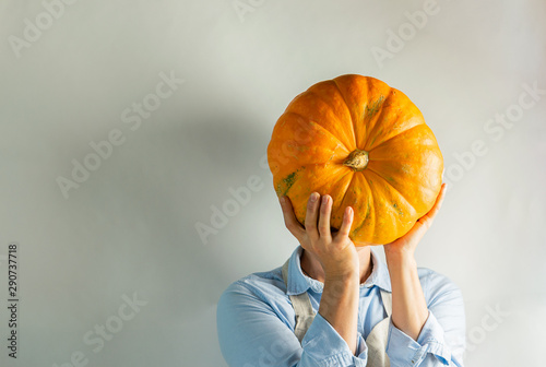 A woman in light clothes holds a large ripe pumpkin instead of a head. Food concept joke. photo