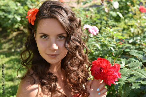 beautiful girl with curls next to red roses in the garden photo