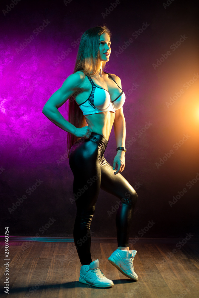 Fototapeta premium Attractive young woman fitness model posing in the studio in neon lights.