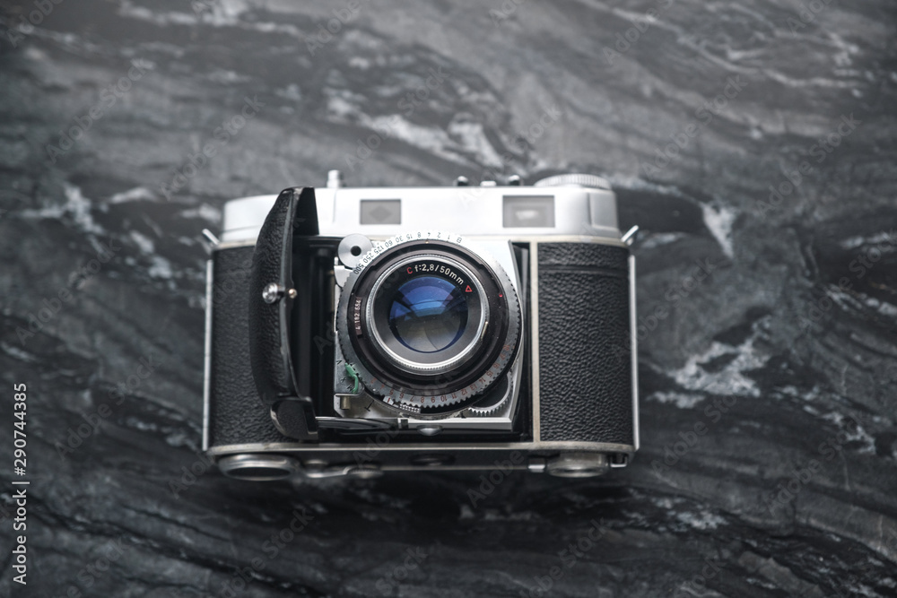 Vintage analog film camera with a lens and a charged film on a marble stone background.