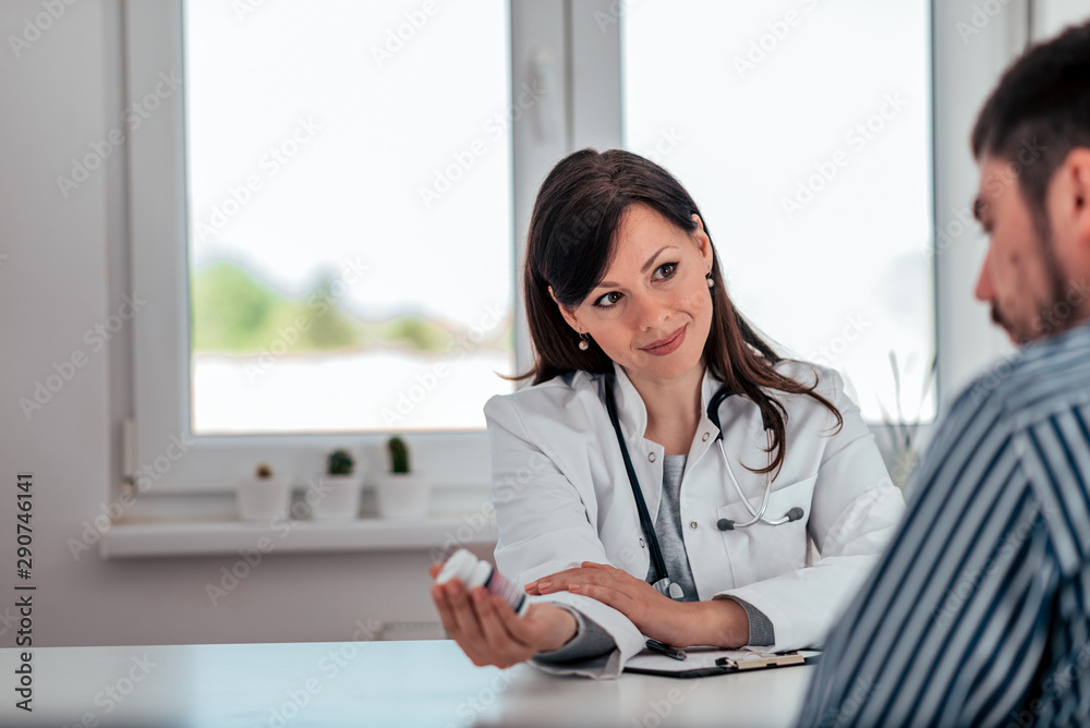 Obraz premium Doctor holding a pill bottle while talking with a patient in the office.