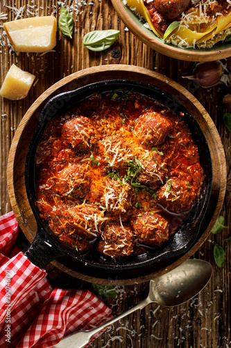 Meatballs in a tomato-herb sauce, sprinkled with parmesan cheese and chopped fresh basil served in a cast iron skillet, close-up, top view.