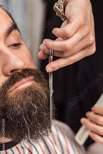 Man getting his beard cut, with scissors, by a female barber, close-up.