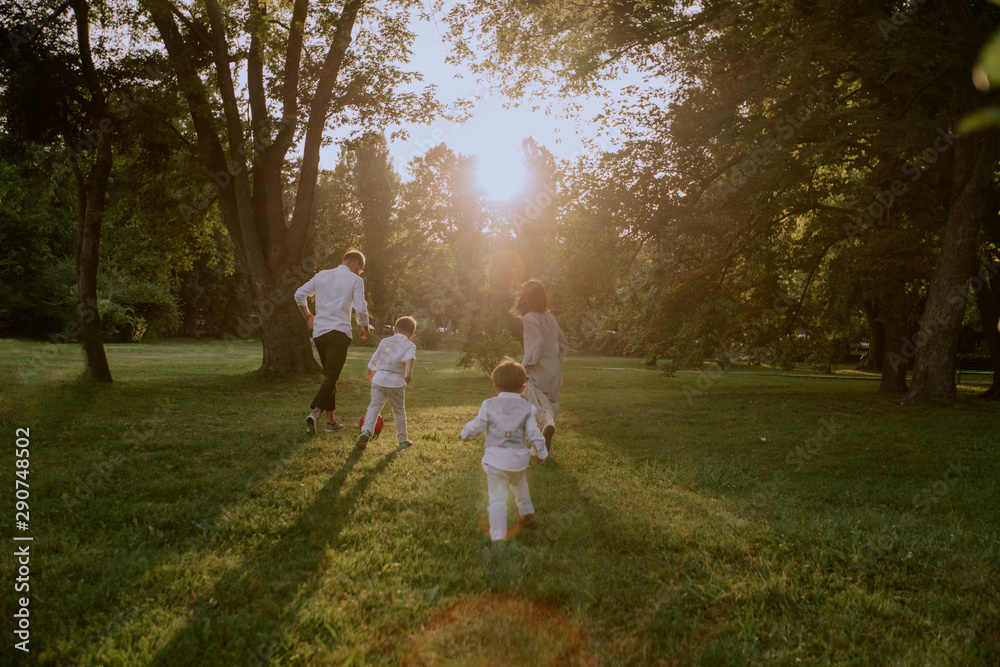 Little cute boys in stylish suits running after their mother and father trying to catch them , they are in the middle of a green park Little cute boys in stylish suits running after their mother and father trying to catch them , they are in the middle of a green park