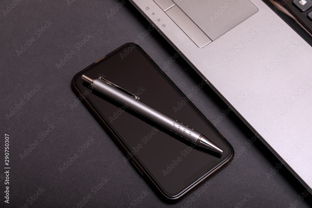 Minimal balck office desk table with laptop, and smarth phone. Top view silver laptop with pen on black table. Minimal balck office desk table with laptop, and smarth phone. Top view silver laptop with pen on black table.