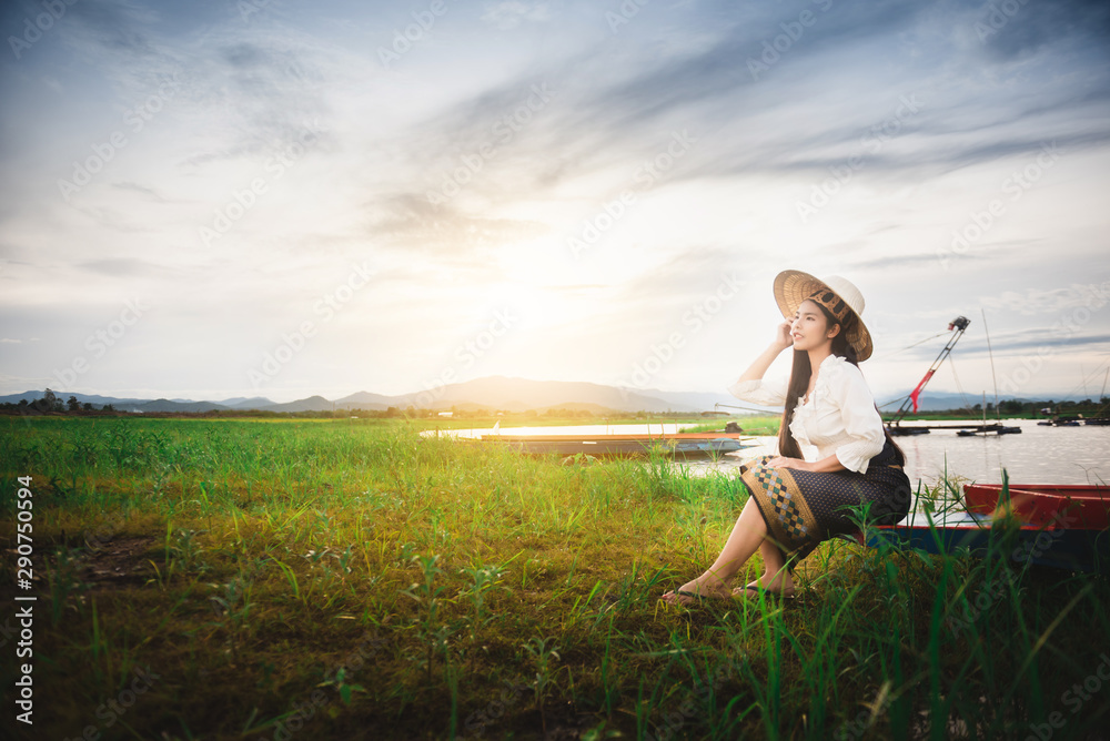 Asian Beautiful woman in Thai local dress sitting on boat in fishing village with field and lake background Asian Beautiful woman in Thai local dress sitting on boat in fishing village with field and lake background