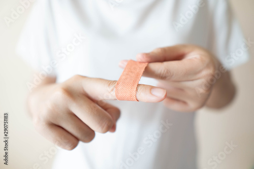 Fotografia Young female in white t-shirt have injured index finger and putting adhesive bandages plaster for first aid