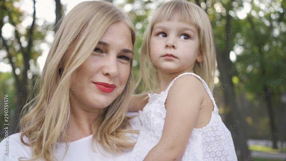 Portrait of young blond woman in white dress caressing her cute daughter. Leisure outdoors. Happy family. One parent. Motherhood, parenthood, happy childhood Portrait of young blond woman in white dress caressing her cute daughter. Leisure outdoors. Happy family. One parent. Motherhood, parenthood, happy childhood