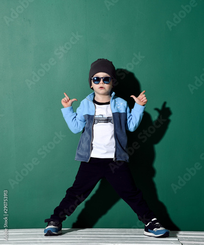 Vászonkép Cool boy in blue sunglasses, headwear, fleece jacket, pants and sneakers is posi