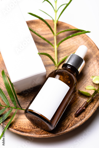 Brown glass cosmetic bottle mock-up with blank white label and green leaves, serum packaging photo