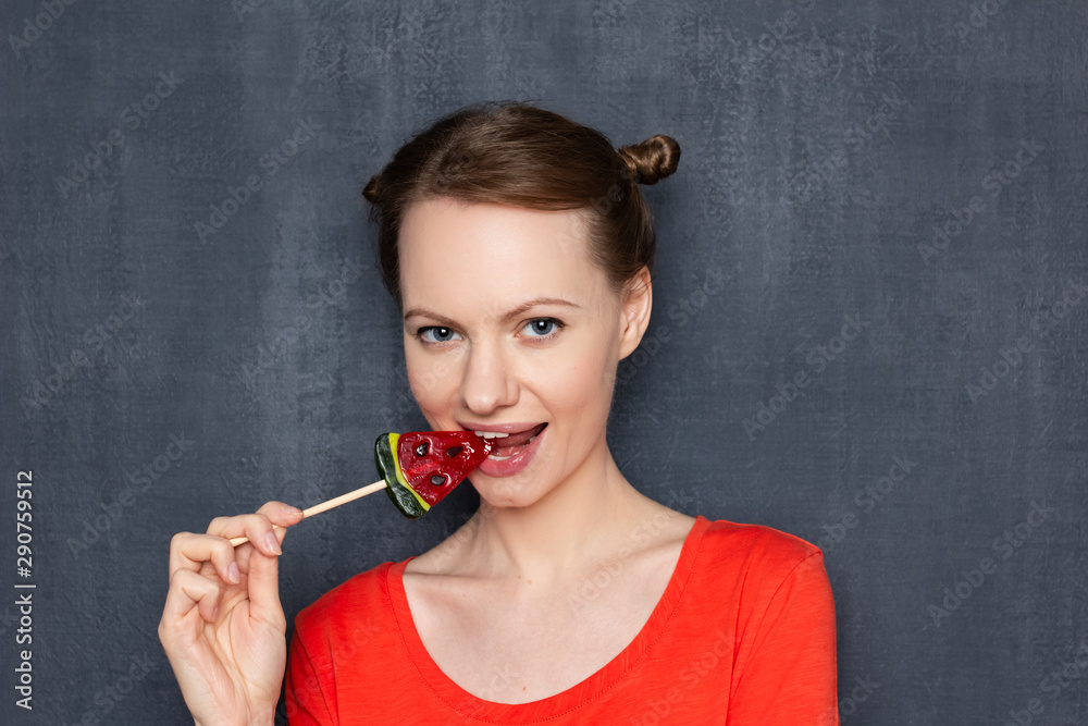 Fototapeta premium Portrait of cute flirty girl biting lollipop and smiling