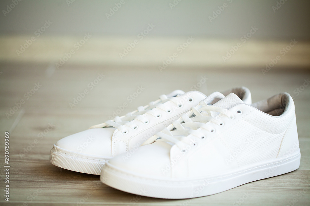Pair of new stylish white sneakers on floor at home Pair of new stylish white sneakers on floor at home