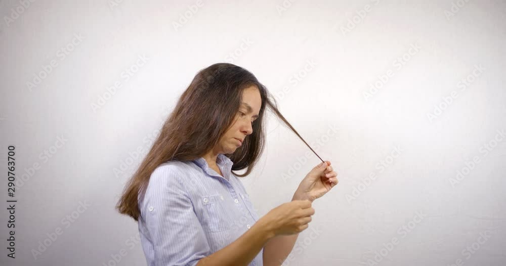 Middle aged woman looks at split ends of her hair on white isolated background Middle aged woman looks at split ends of her hair on white isolated background