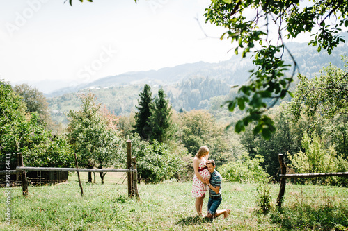 In waiting baby. pregnant woman with beloved husband stand on the grass. round belly. Husband kneeling  embraces wife a round belly. Parenthood. The sincere tender moments. mountains, forests, nature © Serhii