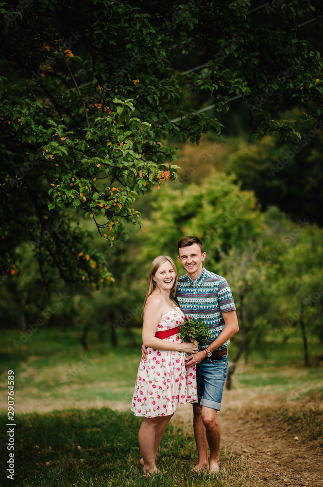 Fototapeta premium In waiting baby. happy family. pregnant woman with beloved husband embrace, barefoot on the grass. round belly. The sincere tender moment. background, nature, park, tree, forest, nine month. happiness