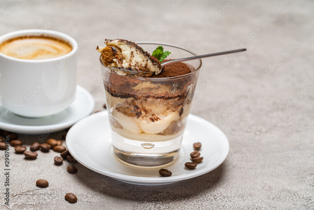 Portion of Classic tiramisu dessert in a glass and cup of coffee on concrete background Portion of Classic tiramisu dessert in a glass and cup of coffee on concrete background