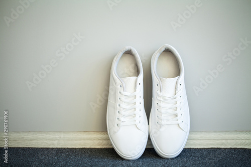 Pair of new stylish white sneakers on floor at home